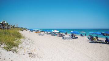 A beach with sun loungers and umbrellas, a lifeguard tower, and the ocean.