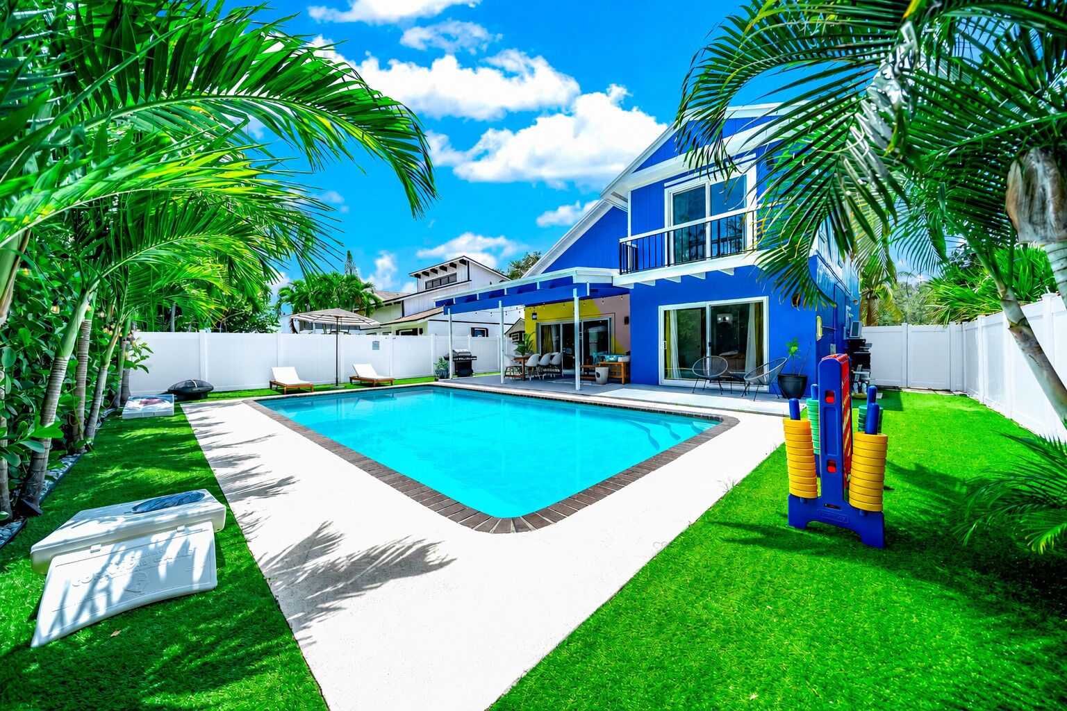 Un jardin avec une piscine, un patio couvert et une maison à la façade bleue.