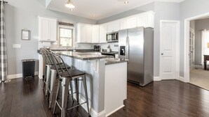 Een moderne keuken met witte kasten, roestvrijstalen apparatuur en een centraal eiland met barstoelen.