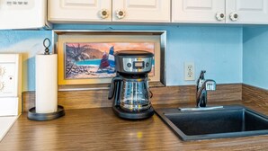 A kitchen with a coffee maker, a candle, and a painting on the wall. - Blue Bungalow on 1st! (Cedar Key)