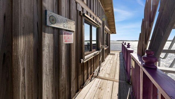 A wooden deck with a fire exit sign, a sign reading "Corbisans Reef," and a view of the beach. - Corrigan`s Reef at Harbour Master Suites (Cedar Key)