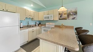 A kitchen with white cabinets, a granite countertop, a microwave, a stove, and a hanging light fixture. - Lucky Catch on 1 Street (Cedar Key)