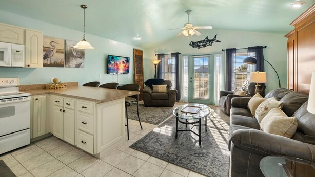 A spacious kitchen with a central island, a dining area with chairs, a living room with a sofa, and a ceiling fan. - Lucky Catch on 1 Street (Cedar Key)