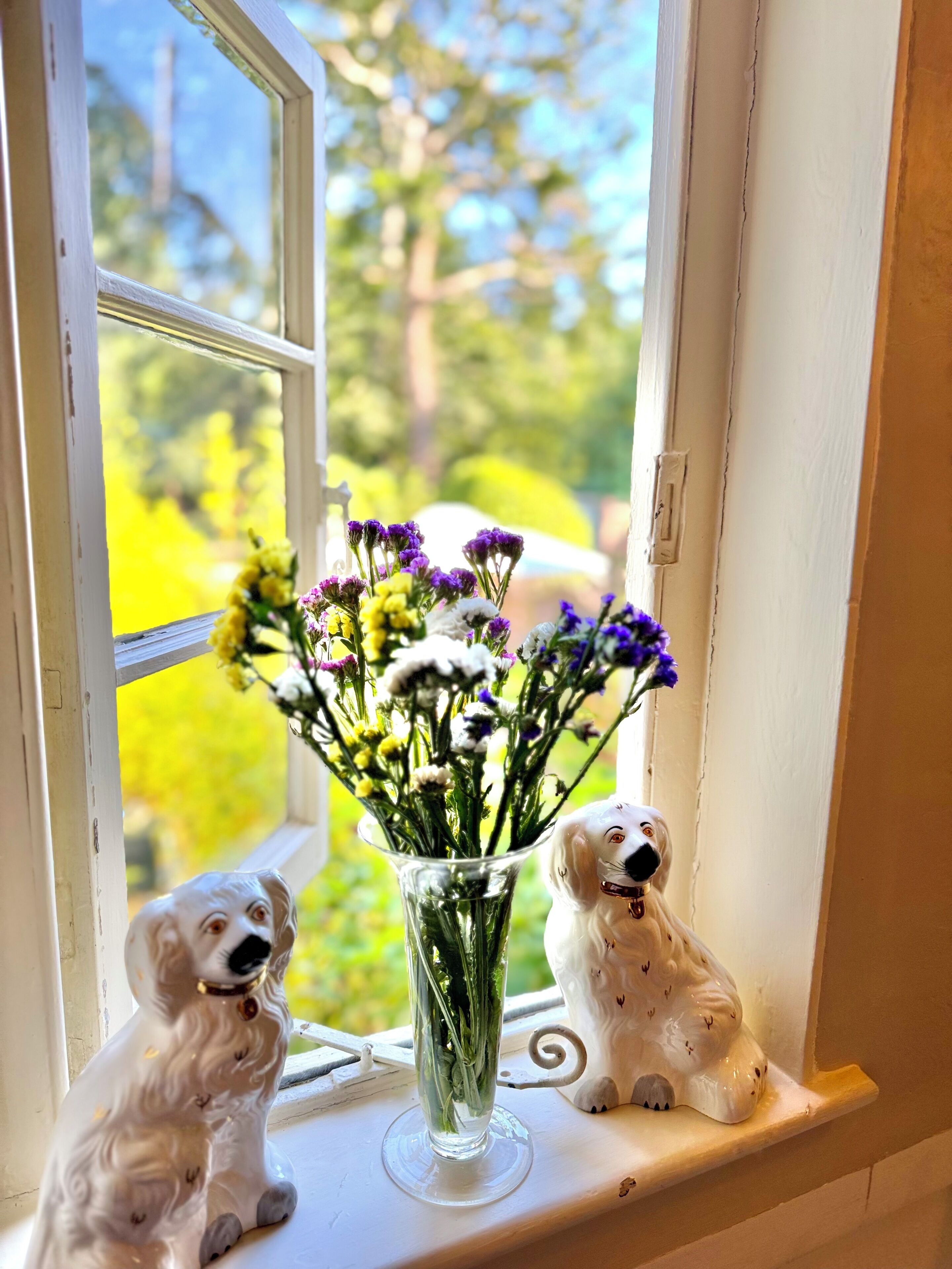 A window sill with a clear vase containing flowers and two dog figurines.