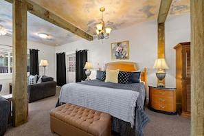 Een slaapkamer met een bed, een dressoir, een nachtkastje, een lamp, een sofa en een raam met gordijnen.