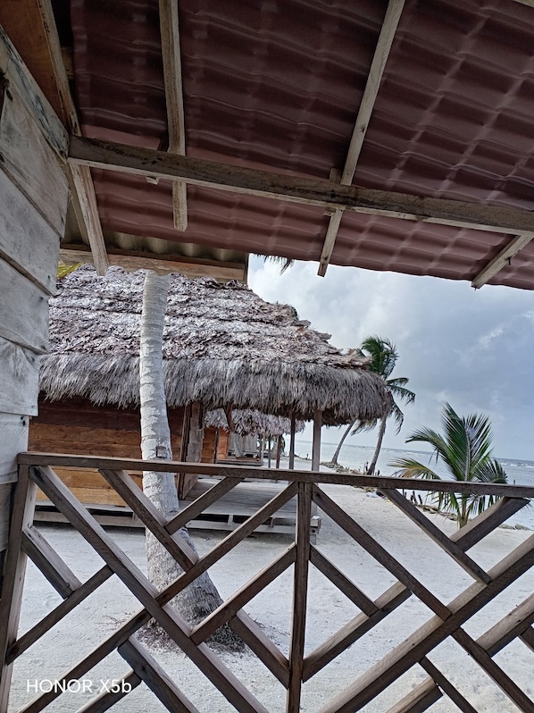 Una cabaña frente al mar con techo de paja, vigas de madera y vistas al océano.