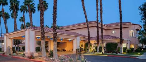 A hotel with a covered entrance, palm trees, and a red-tiled roof.