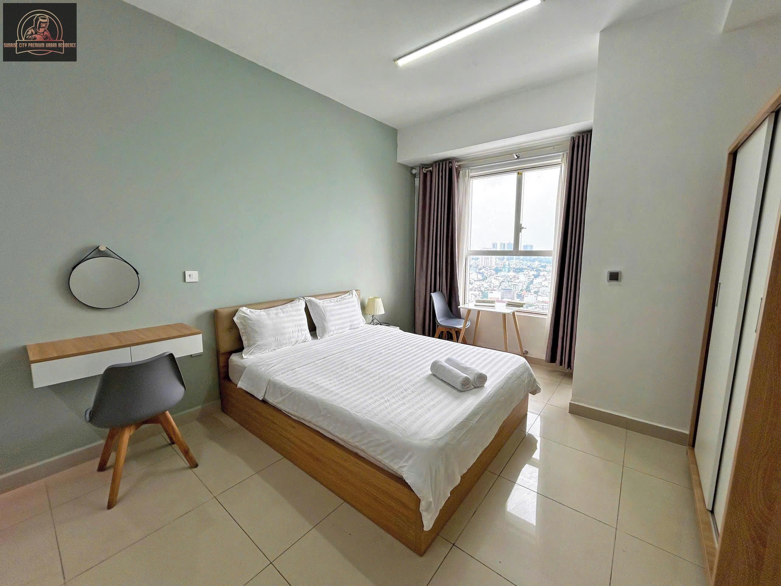 A hotel room with a bed, a desk, a chair, and a view of the city through the window.