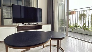 A modern living room with a large flat-screen TV, two round tables, and a balcony with plants. - Sunrise City Premium Urban Residence (Ho Chi Minh City)