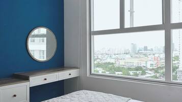 A bedroom with a large window, a round mirror, a bed with white bedding, and a blue accent wall.