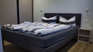 A modern bedroom with a dark-colored bed, grey and white striped bedding, and a small bedside table with a lamp. - Vacation cottage Noa (Twist)