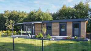 A modern building with a covered patio area, a fenced garden, and a pathway leading to the entrance. - Vacation cottage Noa (Twist)