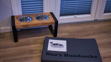 Ein Haustierbett mit dem Aufdruck "Noa's Hundeecce" und eine Holz-Futterstation mit zwei Metallnäpfen.