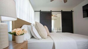 Ein Schlafzimmer mit einem Bett, einem Nachttisch mit Blumenvase, einem Deckenventilator und einer Schiebetür im Scheunenstil.