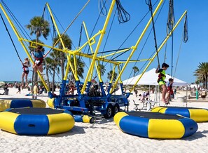 A beach with a blue and yellow structure, possibly a zip line or swing set, and inflatable safety pads on the sand. - Sea Glass Beach Compound | 10BR, Sleeps 28, Near Beach | By Golden Coast Rentals (Clearwater)