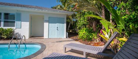 A swimming pool with lounge chairs, a door, and surrounding greenery.