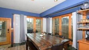 A dining room with a wooden table and chairs, a glass door leading outside, and a shelf with items on the right.