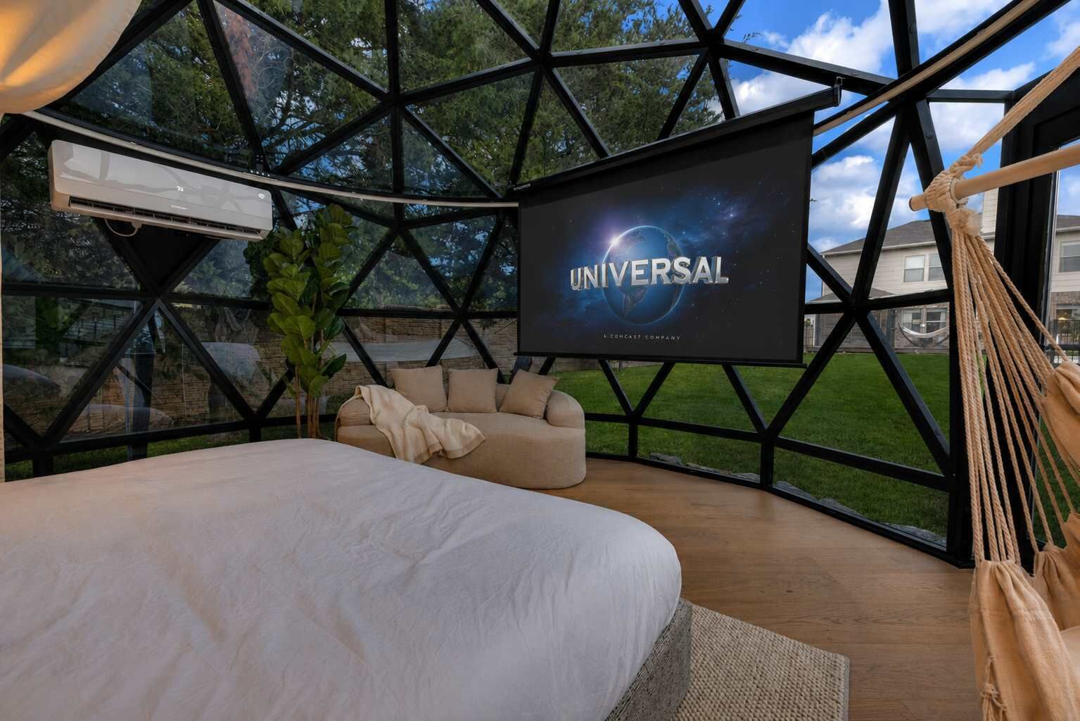 Een moderne kamer met een groot bed, een televisiescherm waarop 'UNIVERSAL' staat en een hangstoel.