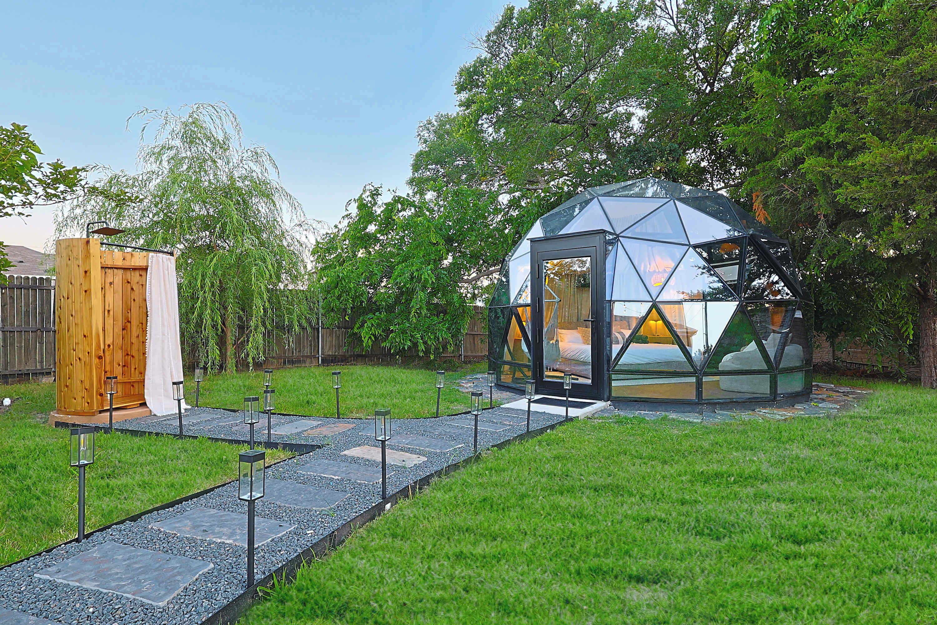 Una struttura a cupola geodetica con un ingresso in vetro, una sauna in legno e un sentiero in pietra che vi conduce.