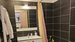 Ein Badezimmer mit dunkel gefliesten Wänden, einem weißen Waschbecken, einem Spiegel und einer Duschkabine mit Vorhang.