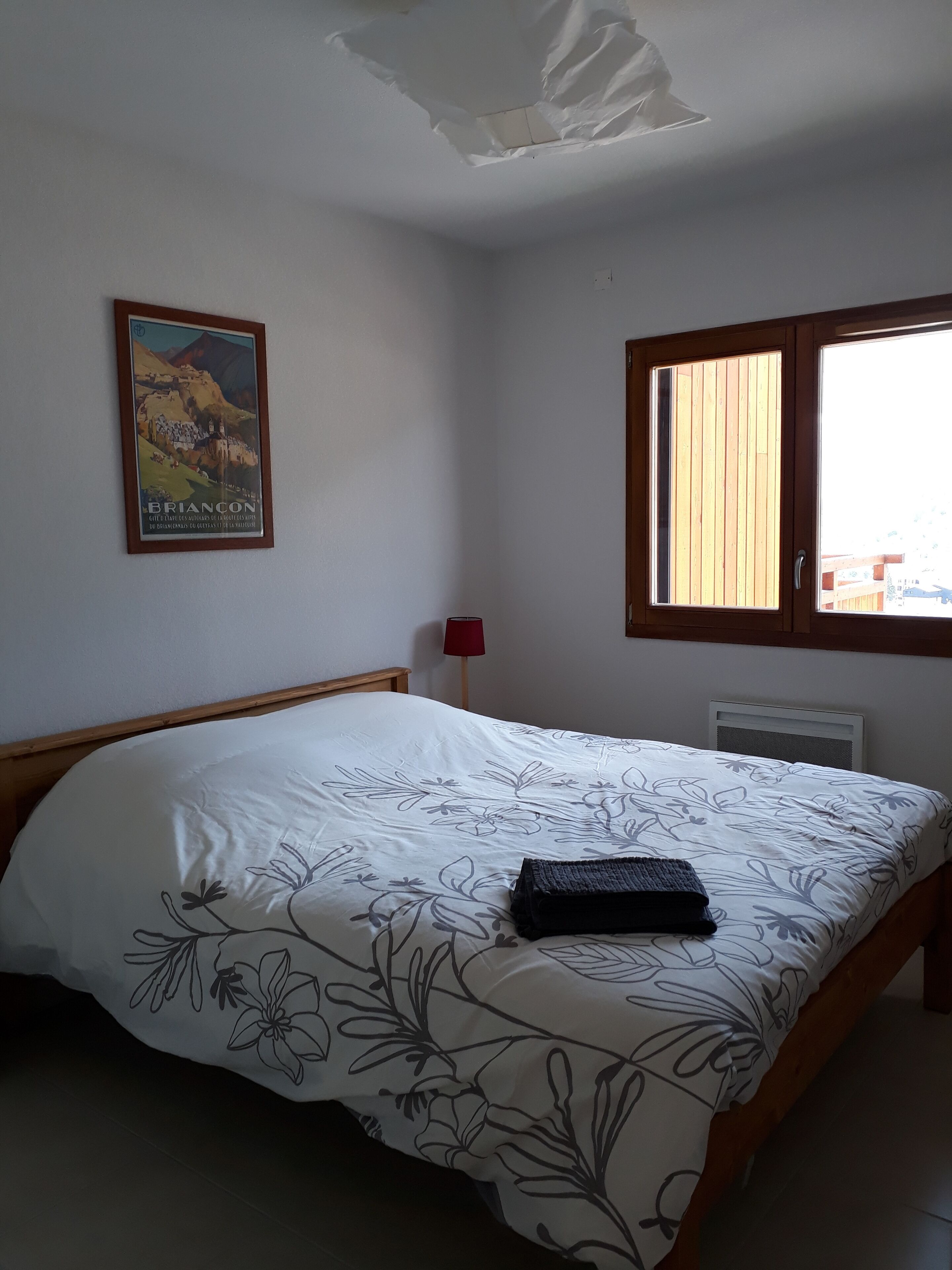 Une chambre à coucher avec un lit, une affiche au mur, une fenêtre et une lampe rouge.