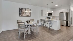 Eine moderne Küche mit weißen Schränken, einem Edelstahlkühlschrank und einem Essbereich mit rundem Tisch und Barhocker.