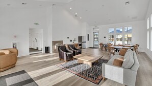 Ein geräumiger Wohnbereich mit Sofa, Sesseln, einem Couchtisch und einem Esstisch mit Stühlen. Es gibt eine Küchenzeile mit Kühlschrank und Spüle. Das Zimmer verfügt über große Fenster und eine hohe Decke.