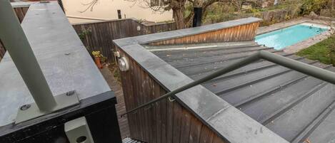 A rooftop with a pool, wooden deck, and a metal railing.