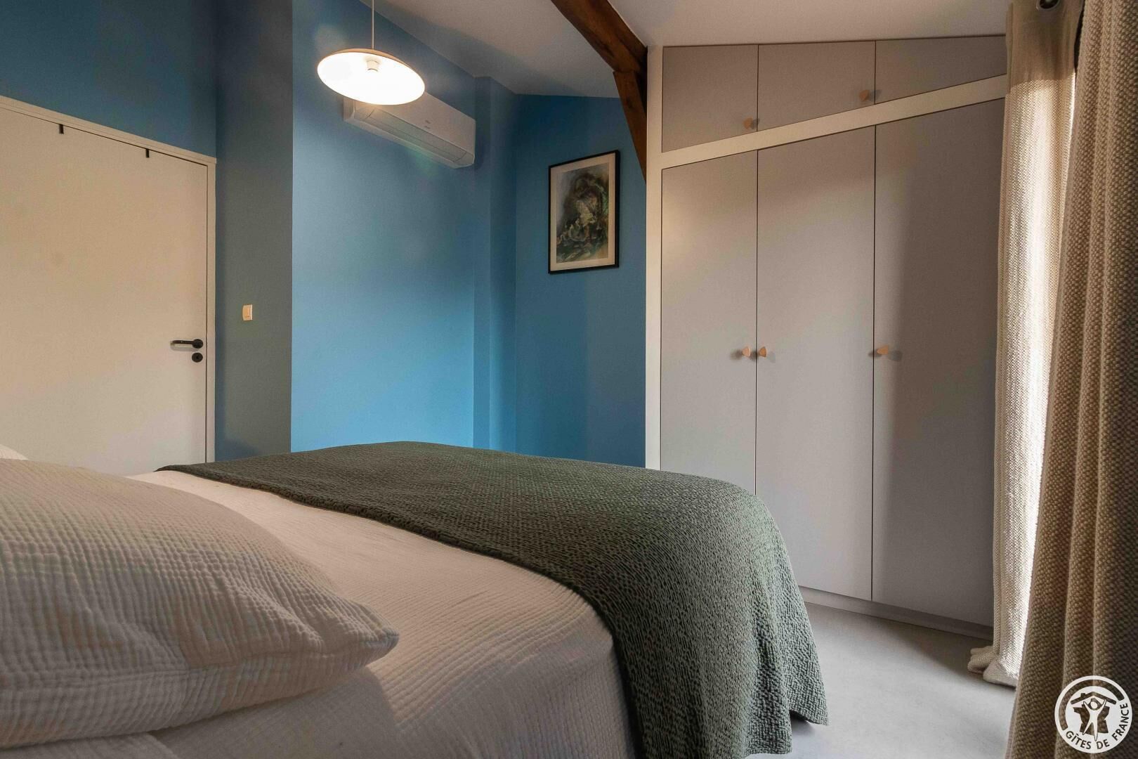 A bedroom with a bed, a wardrobe, and a painting on the wall.