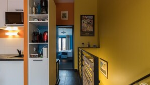 A hallway with a kitchen area on the left, a bed in the middle, and a staircase leading to another floor. - Oyasumi - MURET - Gîte (MURET)