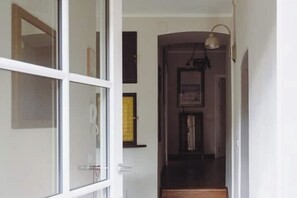 Ein Flur mit Glastür zu einem Zimmer, einer dunklen Holztreppe und einer wandmontierten Leuchte.