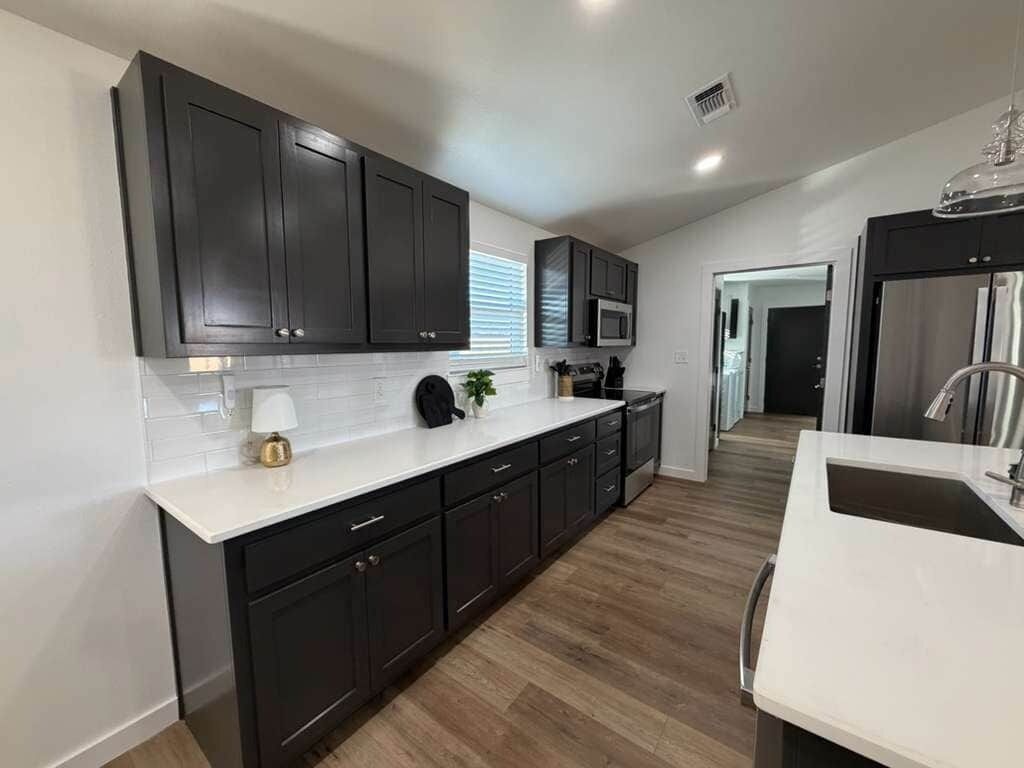 A modern kitchen with dark cabinets, a white countertop, and a stainless steel refrigerator.
