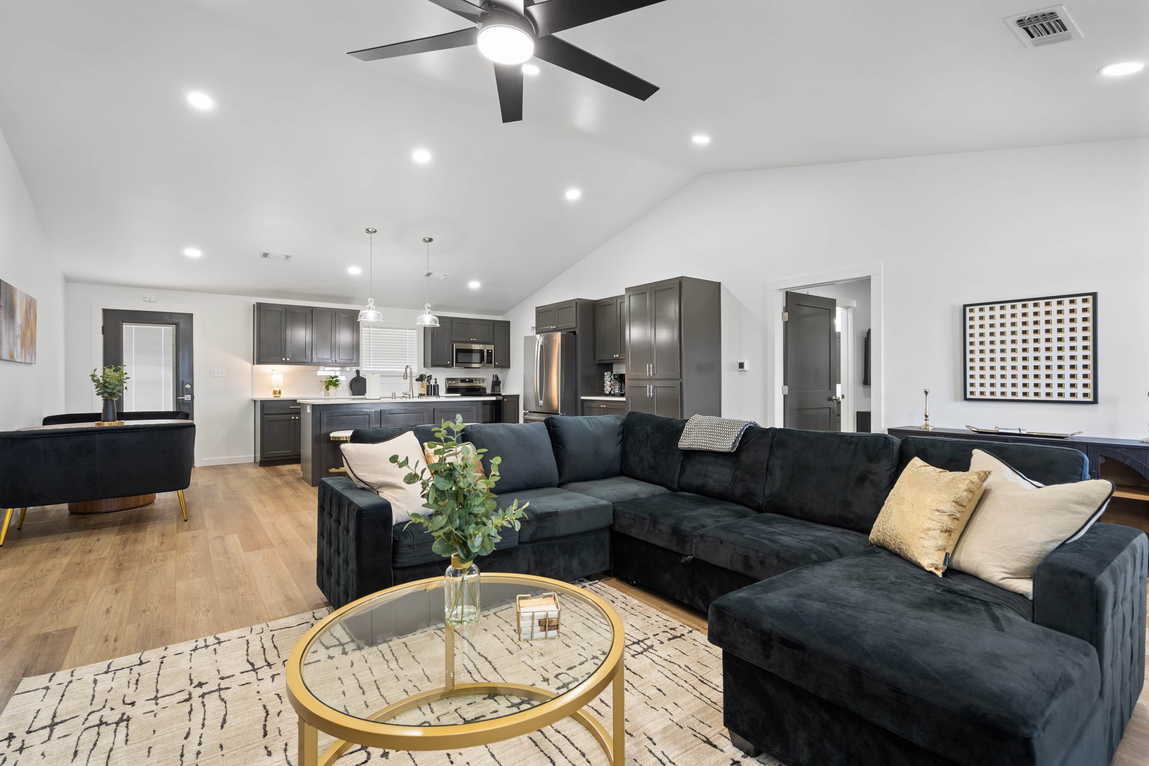 A modern living room with a dark sectional sofa, a glass coffee table, and a dining area with a black table and chairs.