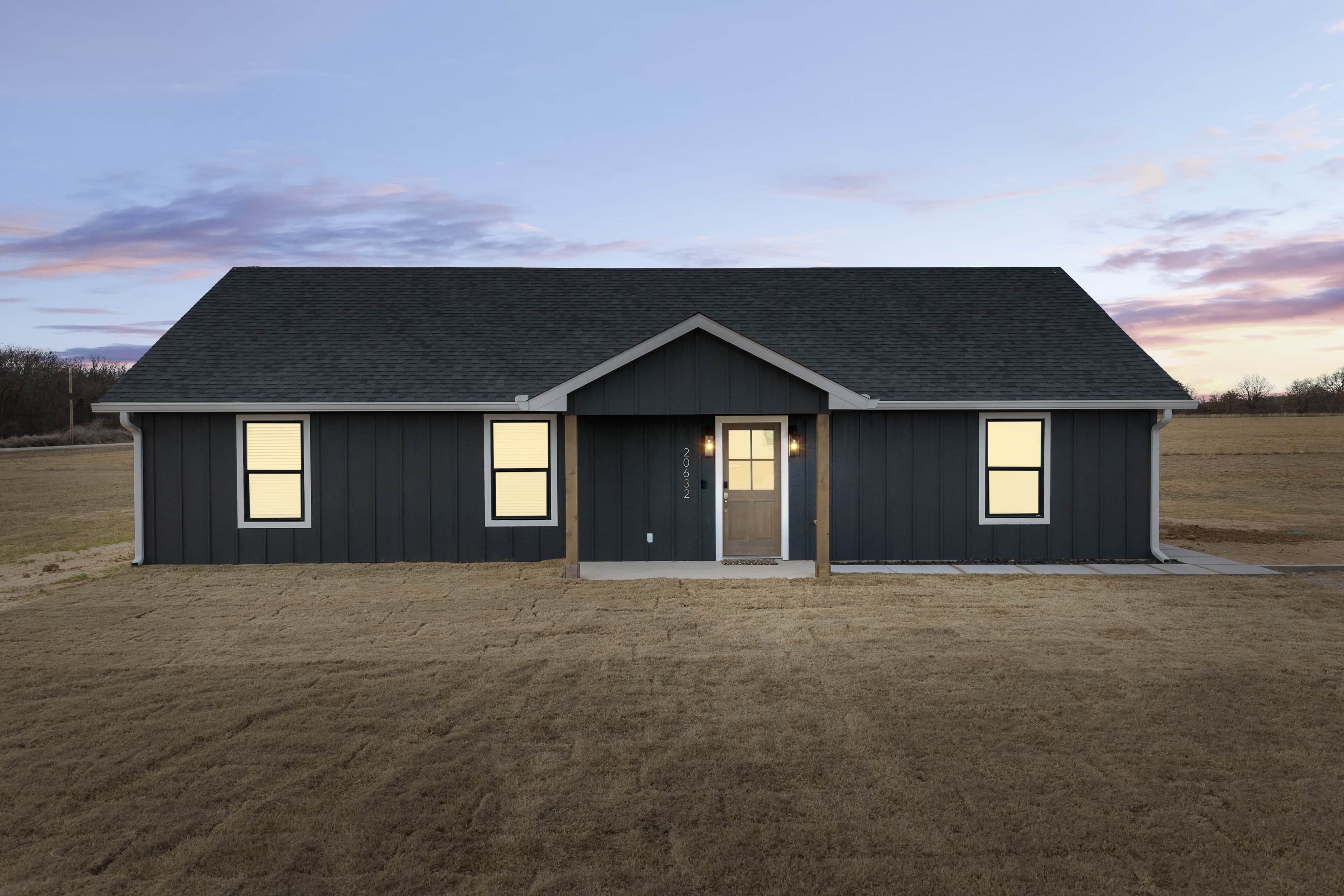 A modern two-story house with a dark exterior, a front door, and three windows.