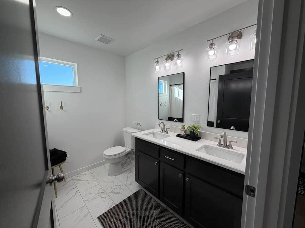 Une salle de bain moderne avec des toilettes blanches, un meuble-lavabo à deux vasques et un grand miroir.