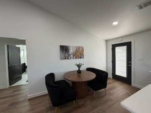 A modern room with a round wooden table, two black chairs, a painting on the wall, and a door with blinds. - Royal Flush Villa - King Bed near WinStar (Thackerville)