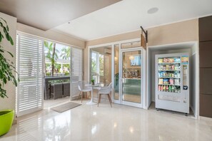A modern indoor space with a seating area, a vending machine, and a glass door leading to an outdoor area. - Beach View - Eagle's Nest Luxury 2BR condo - LV508 (Eagle Beach)