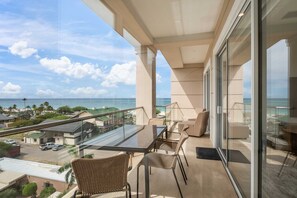Un balcone con un tavolo e sedie in vetro, vista su spiaggia e oceano.