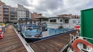 A boat docked at a pier with a wooden deck, surrounded by buildings. - L'Escapade - RAMONVILLE SAINT AGNE (RAMONVILLE SAINT AGNE)