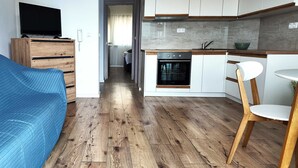 A modern kitchen with wooden cabinets, a built-in oven, and a dining area with a wooden chair. - Apartment Azure Suite in Lokva Rogoznica (Lokva Rogoznica)