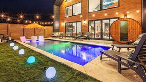 Ein modernes Haus mit Pool, Sitzgelegenheiten im Freien und einer Holzterrasse.
