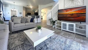 Una sala moderna con un sofá, una mesa de centro y un televisor grande sobre un mueble blanco.