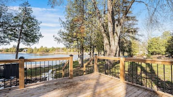 Eine Holzterrasse mit Geländer, die auf einen See mit umliegenden Bäumen und einem Steg blickt.