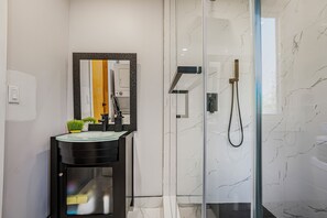 Een moderne badkamer met een douchecabine van glas, een zwarte wastafel met spiegel en marmeren wanden.