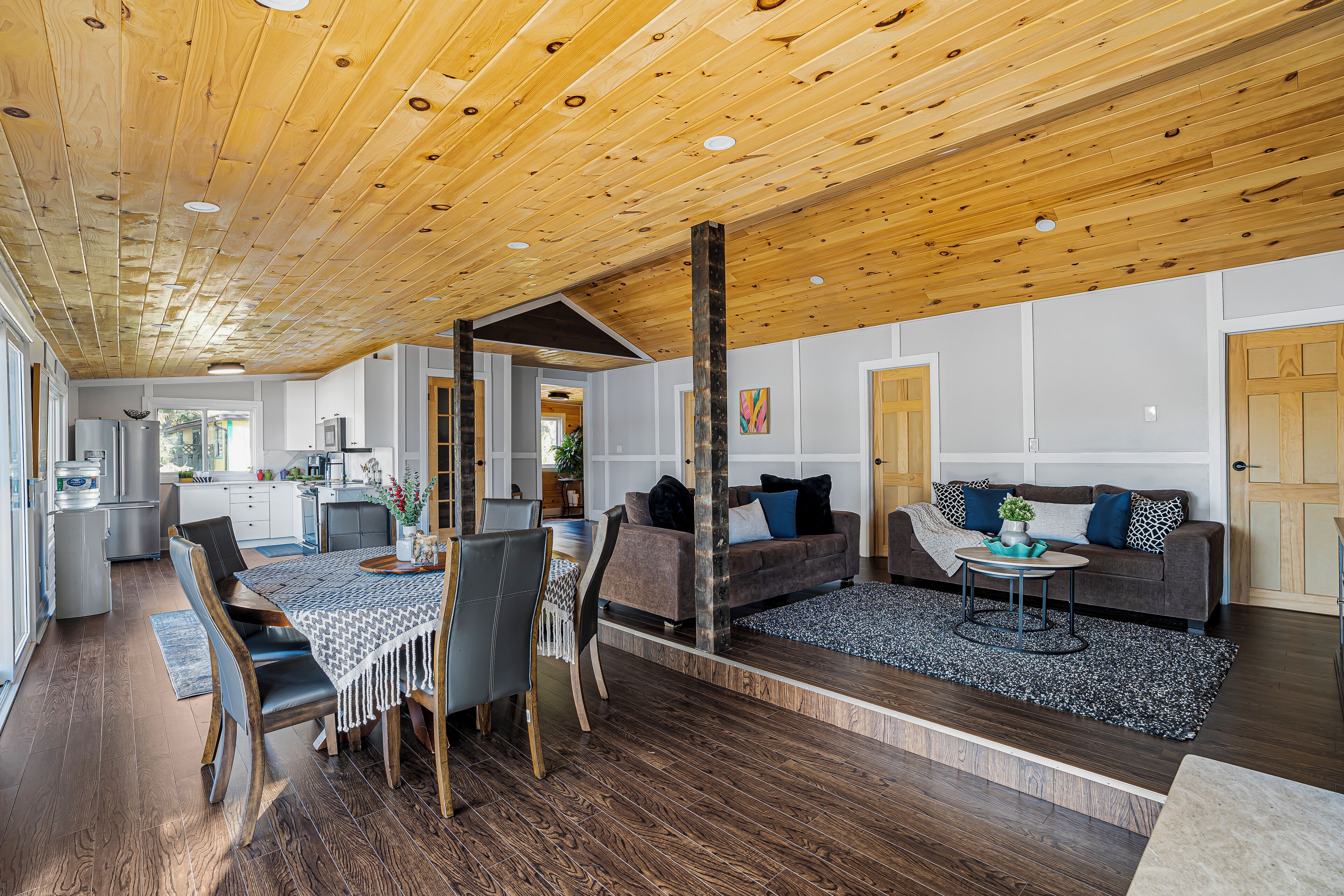 Un amplio salón con techo de madera, una mesa de comedor con sillas, un sofá y una cocina al fondo.