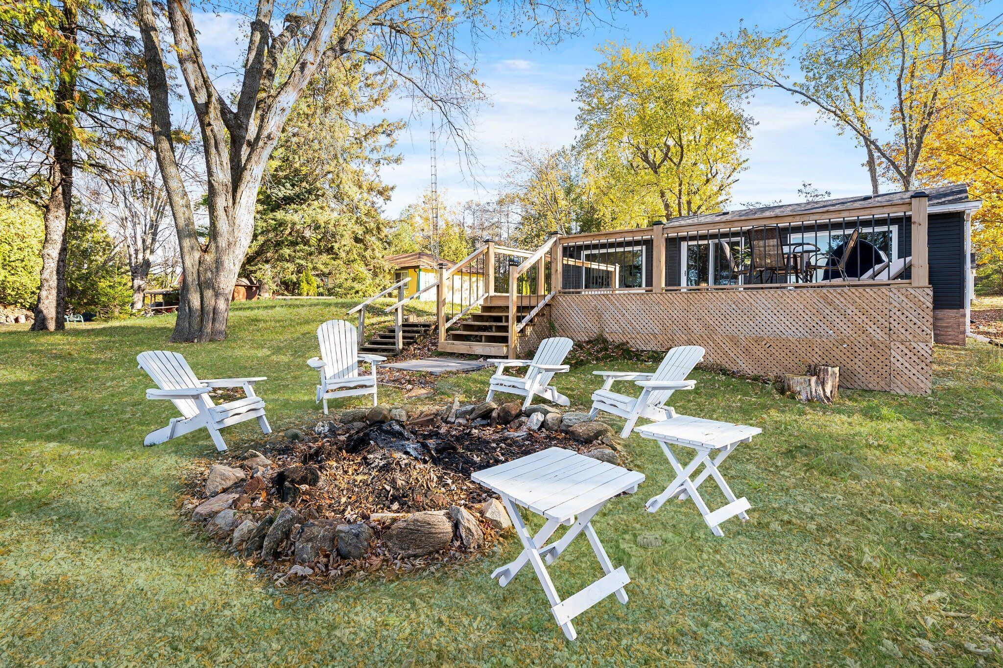 A cozy outdoor seating area with Adirondack chairs and a fire pit, surrounded by a wooden deck and a large window overlooking a garden.