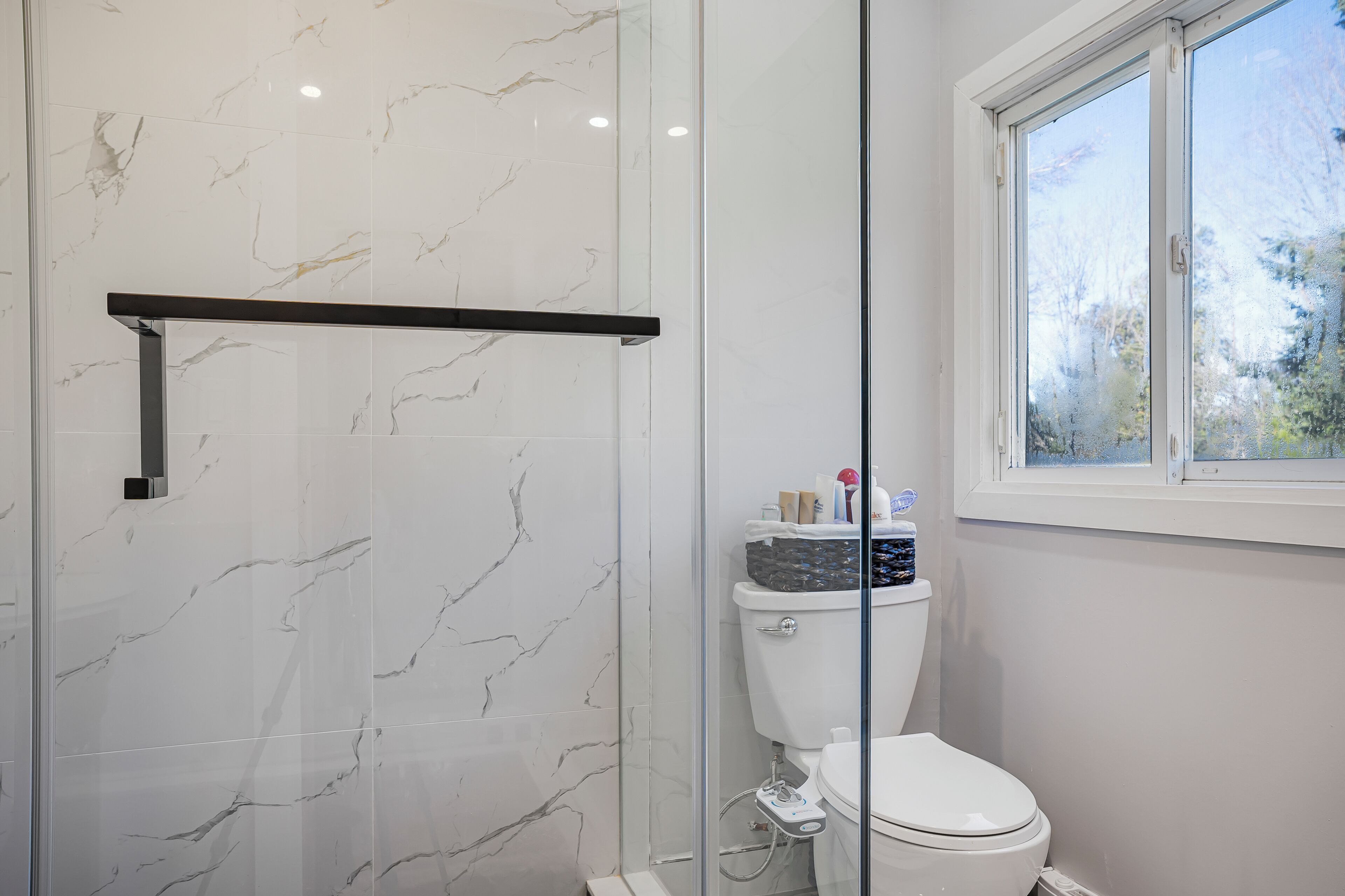 A bathroom with a glass-enclosed shower, a toilet, and a window providing a view of trees.