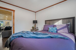 Een slaapkamer met een groot bed, een nachtkastje met een lamp, en een stoel in de aangrenzende kamer.
