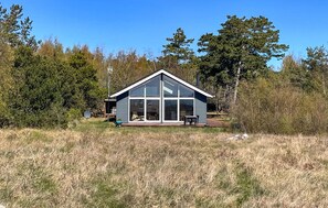 Ein modernes Haus mit großen Glasfenstern, einer Terrasse mit Gartenmöbeln und einer Satellitenschüssel.