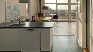 Una cocina moderna con lavavajillas, un comedor con sillas y mesa, y un amplio ventanal con vistas al campo.